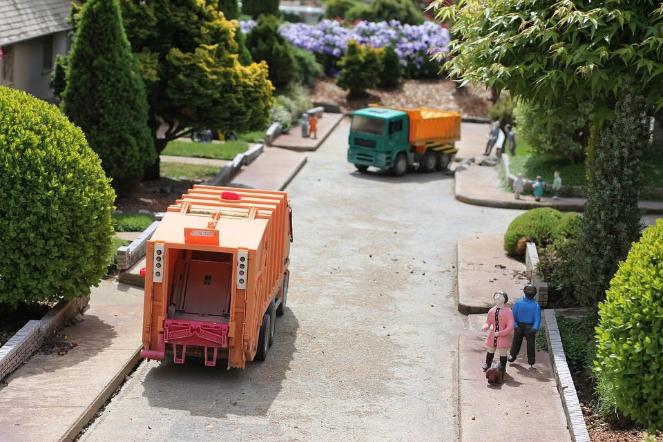 A miniature model of a street with two toy garbage trucks and toy people, symbolizing garbage collection.